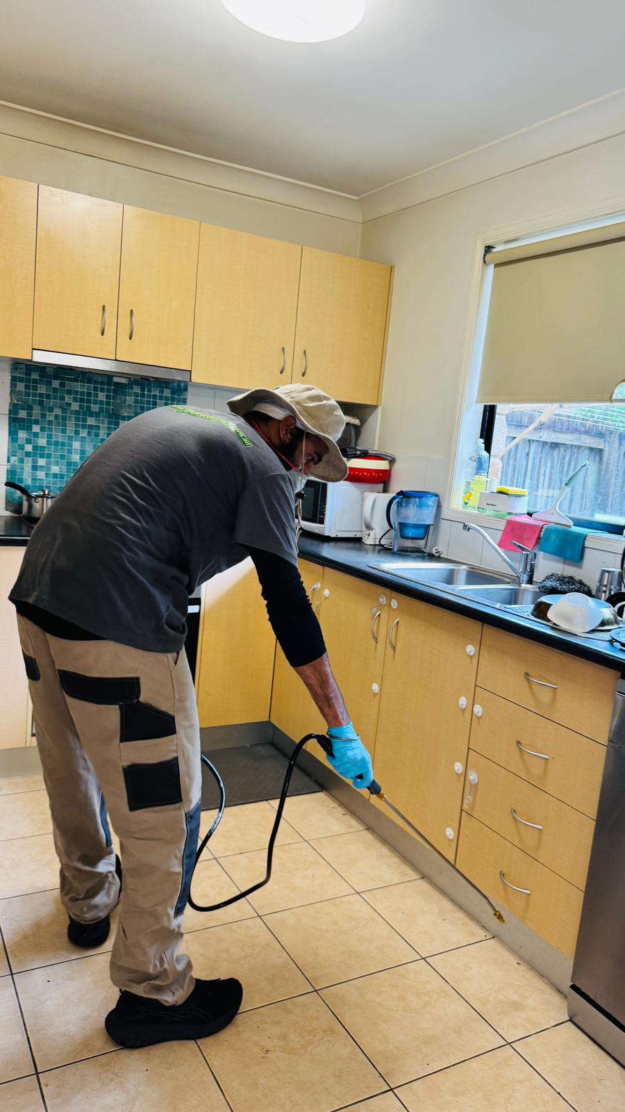 Pestigo technician performing pest treatment along kitchen cabinet baseboards